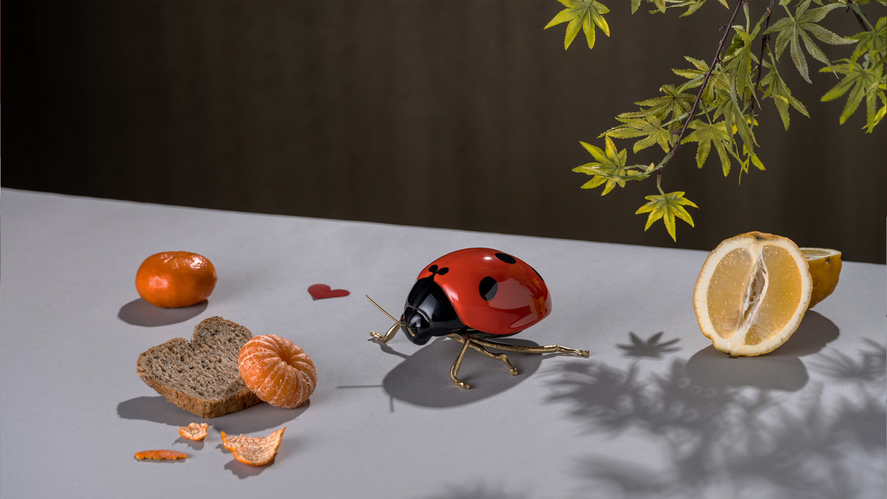 joaninha de cerâmica e latão numa mesa com tangerinas e limões