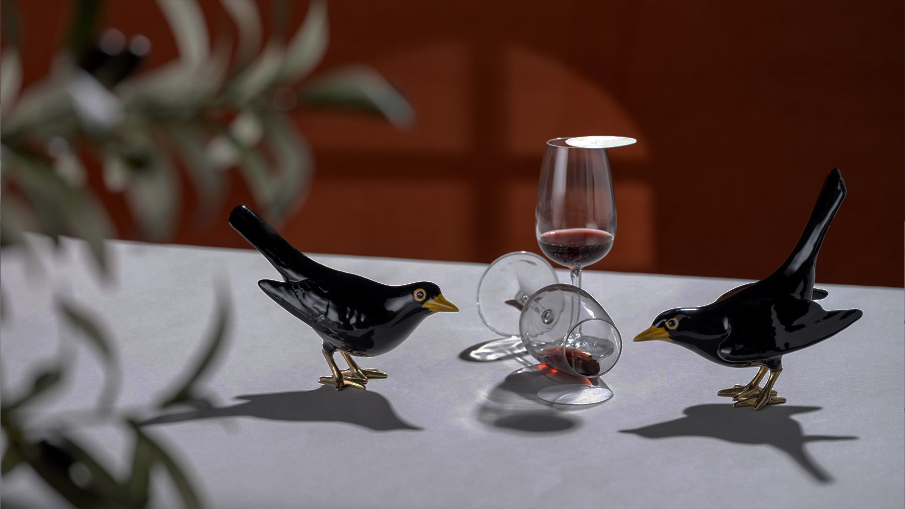 dois melros de cerâmica e latão numa mesa junto a dois copos de vidro com vinho